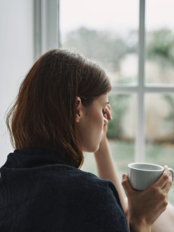Depressed Woman Holding Coffee Cup Sitting By Window